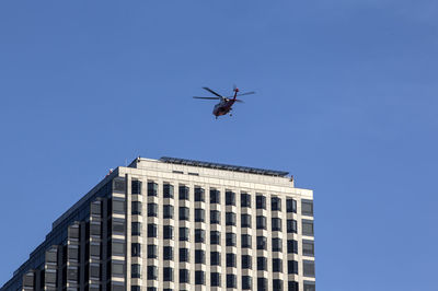 Low angle view of helicopter flying over modern building against blue sky