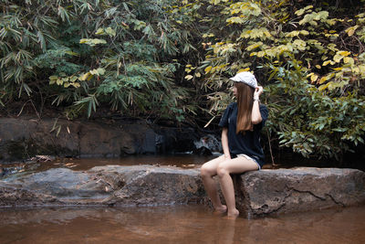 Woman sitting on plant against trees