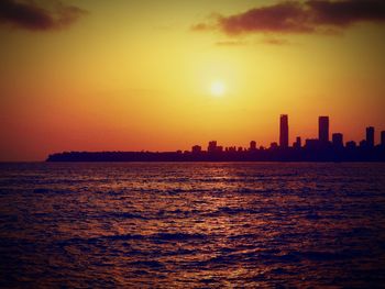 Silhouette city by sea against sky during sunset