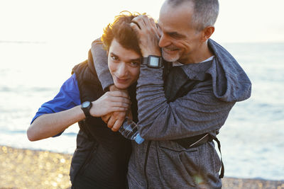 Portrait of happy son with playful father holding head at beach