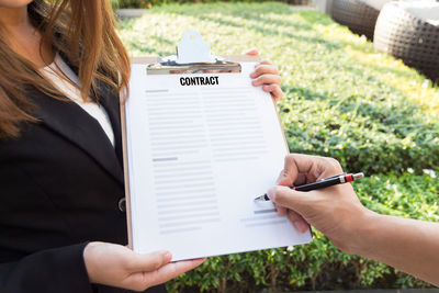 Cropped hand signing contract held by businesswoman in yard