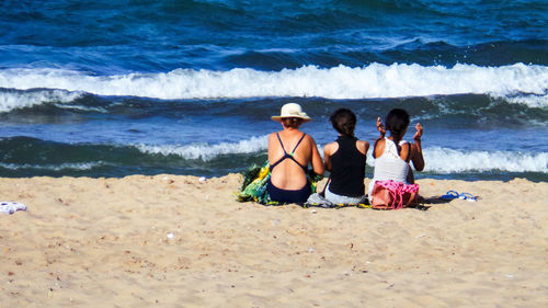 Rear view of friends sitting on beach against sea