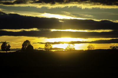 Silhouette trees on landscape against sunset sky