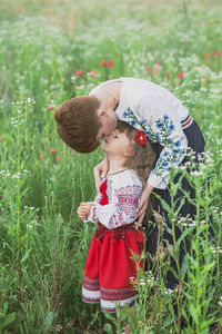 Mom in ukrainian national dress kisses her daughter in a field with flowers
