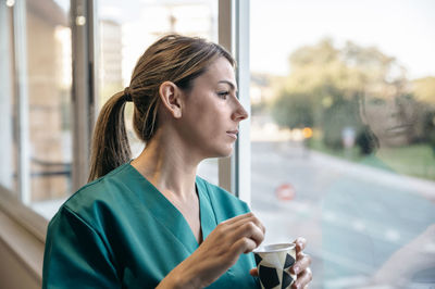 Woman in scrubs having coffee break looking out of the window