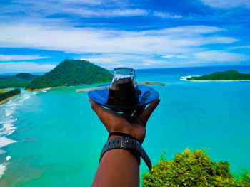 Midsection of person holding sea against blue sky