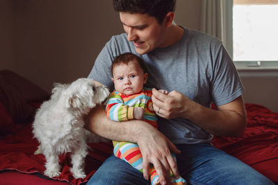 Man sitting with baby boy and dog on bed at home