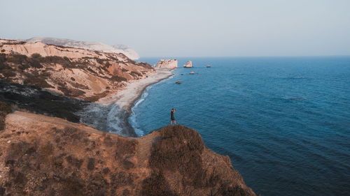 Distant view of man standing by cliff looking at sea
