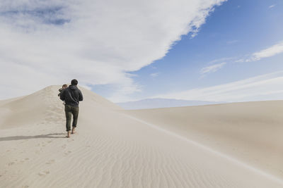 Rear view of man walking on desert against sky