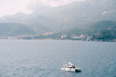 Sailboats sailing on sea by mountains against sky