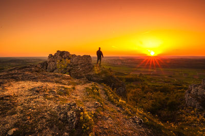 Man standing on rock against orange sky