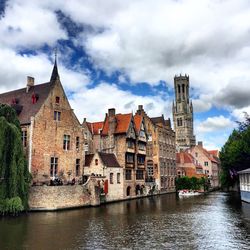 Canal by buildings against cloudy sky