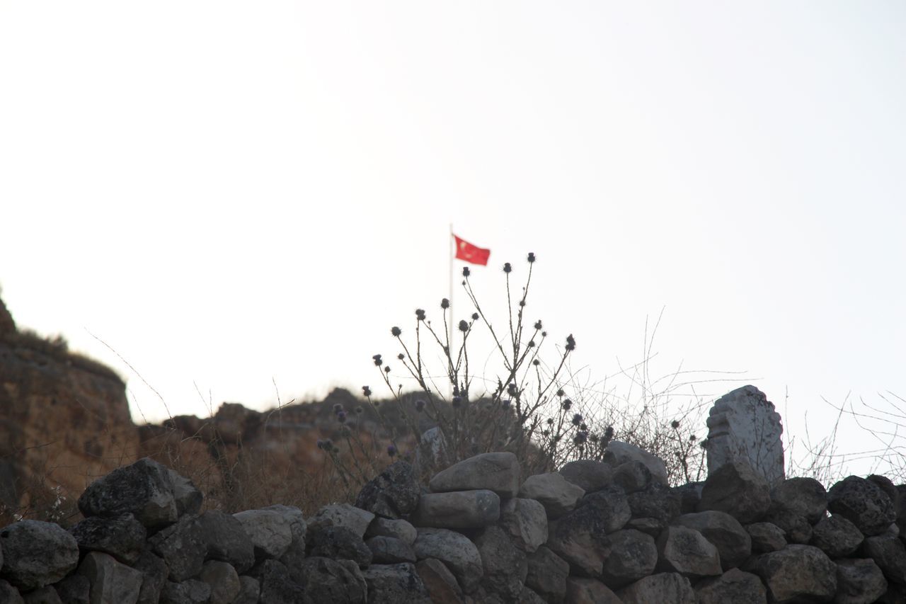 clear sky, low angle view, copy space, flag, rock - object, sky, red, nature, rock, rock formation, day, no people, tranquility, outdoors, beauty in nature, identity, guidance, tranquil scene, growth, patriotism