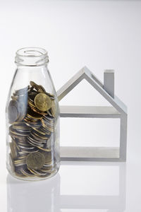 Close-up of model home and coins jar over white background