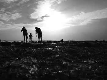 Silhouette people on beach against sky during sunset