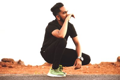 Young man looking away on road against clear sky