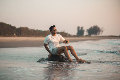 Young good looking man sitting on a rock at the beach during sunset