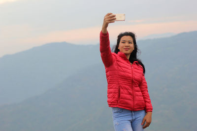 Young woman talking selfie against mountain and sky