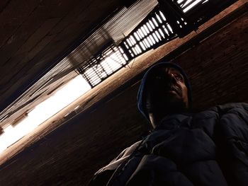 Low angle view of young man looking away while standing against wall