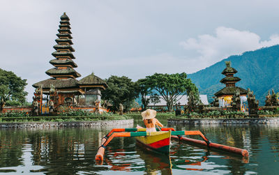 Woman in outrigger at pura ulu danau temple against sky