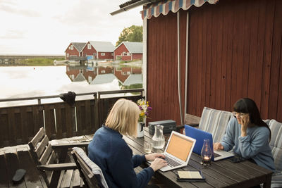 Women using laptop at table in holiday villa by lake