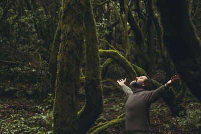 Rear view of woman sitting on tree trunk in forest