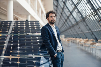 Businessman with hands in pockets leaning on solar panel