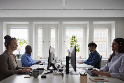 Men and women working in office, using pc desktops while talking via headset