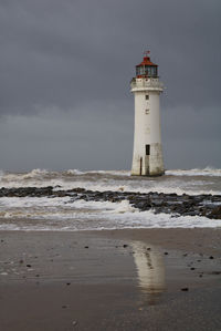 Lighthouse on beach by sea against sky