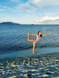 Gymnast standing on beach by sea against sky