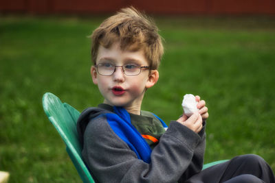 Boy holding food while sitting on chair over grass