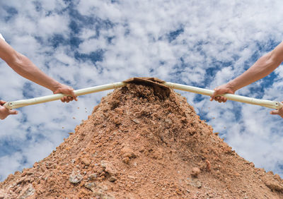 Multiple image of worker holding shovel on dirt heap against sky