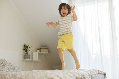 A little boy joyfully jumps on the bed in the bedroom. fun games at home. 