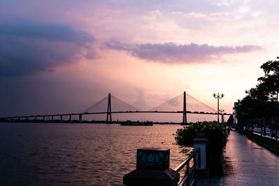 Silhouette bridge over calm river against sky