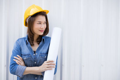 Young woman looking away while standing against wall