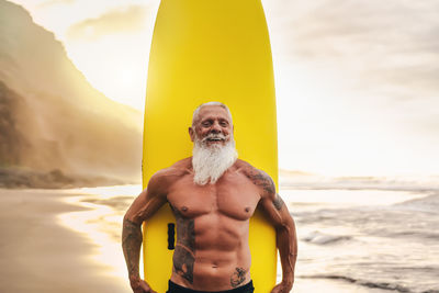 Portrait of shirtless man holding surfboard against sea