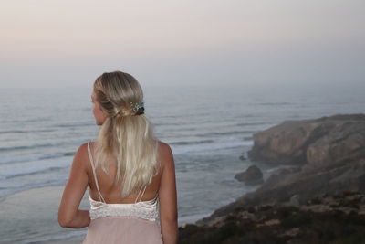 Rear view of woman standing at sea shore against sky