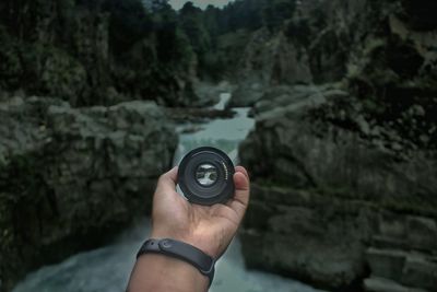 Cropped hand holding camera against waterfall