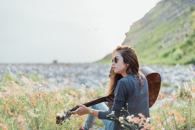 Woman with guitar sitting on field