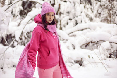 Woman enjoy in pink clothes a jacket a knitted scarf and a hat stands in a snowy forest in winter