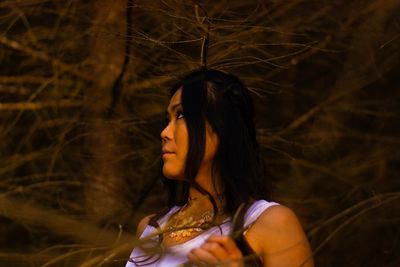 Young woman looking away against trees at night