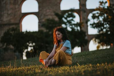 Woman sitting on field against built structure