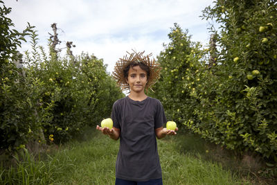 Portrait of smiling boy holding apple against trees