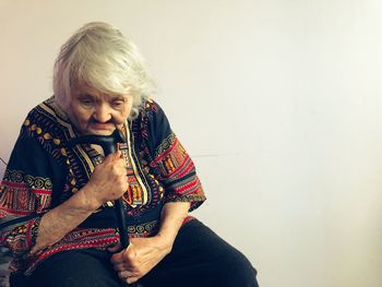 Close-up of senior woman holding walking cane while sitting by wall