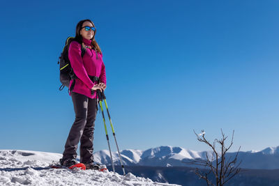 Snow hiker in the mountains, with snowshoes, snow poles and backpack. middle-aged woman, full length
