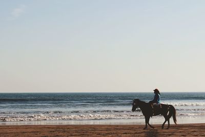 Man riding horse on beach against sky