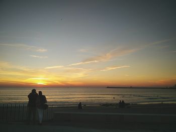 Silhouette people on beach against sky during sunset