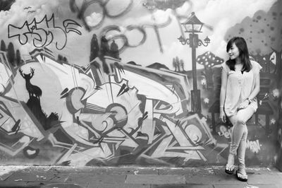 Smiling woman leaning on graffiti over wall