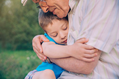 Grandfather and grandson embracing while sitting at park