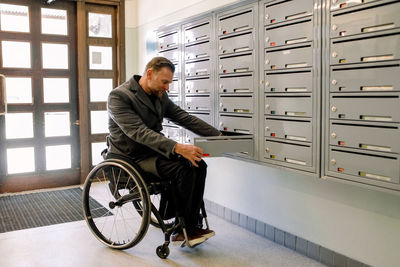 Full length of disabled mature man opening mailbox in locker room while sitting on wheelchair